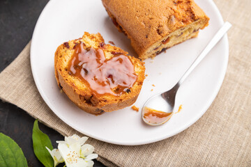 Homemade cake with raisins, almonds, soft caramel and a cup of coffee on a black concrete background. Side view, selective focus.