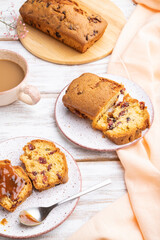 Homemade cake with raisins, almonds, soft caramel and a cup of coffee on a white wooden background. Side view, close up.