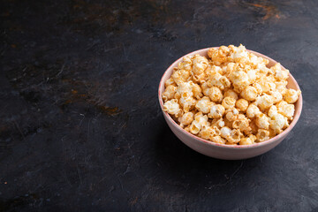 Popcorn with caramel in ceramic bowl on a black concrete background. Side view, copy space.
