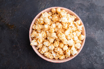Popcorn with caramel in ceramic bowl on a black concrete background. Top view, close up.