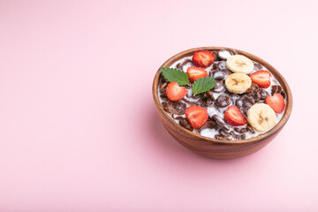 Chocolate cornflakes with milk and strawberry in wooden bowl on pink background. Side view, copy space.