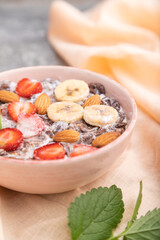 Chocolate cornflakes with milk, strawberry and almonds in ceramic bowl on gray concrete background. Side view, selective focus.