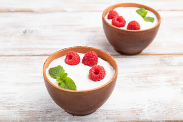 Yogurt with raspberry in clay cups on white wooden background. Side view.