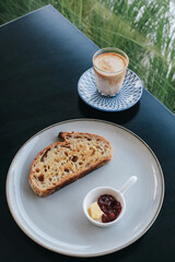 Freshly homemade baked sour dough rye bread sliced and served with jam and butter on white plate and coffee late.