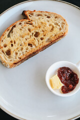 Freshly homemade baked sour dough rye bread sliced and served with jam and butter on white plate.