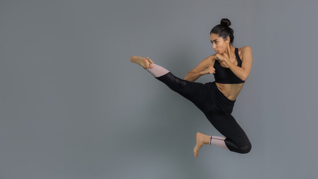 Joven mujer latina mexicana atleta entrenando artes marciales: taekwondo, karate, box. Vestida de negro y haciendo ejercicio con fondo gris