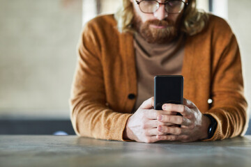 Minimal cropped shot of bearded man using mobile phone with focus on male hands holding smartphone,...