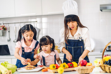 Portrait of enjoy happy love asian family mother and little asian girl daughter child having fun cooking together with fresh vegetable salad and sandwich ingredient on table in kitchen