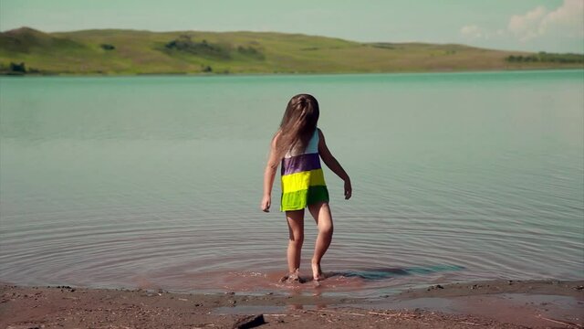the girl is trampling in the water near the river. a child plays by the pond