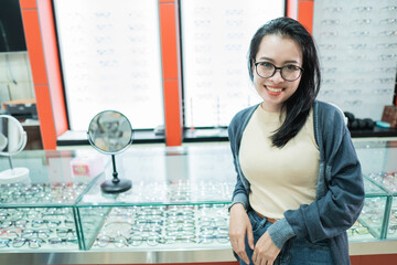 a beautiful woman wearing glasses of her choice and posing in front of an eyeglass window at an eye...