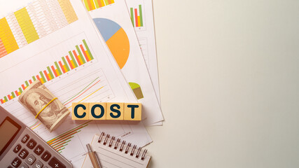Text COST on wooden block over graph, calculator, dollar bill, saving money wealth, business stuff, personal financial, finance accounting concept.
