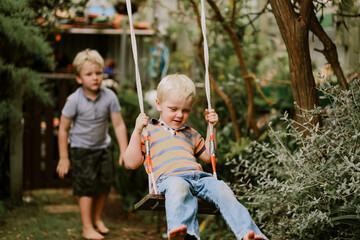 Beautiful happy brothers playing together on backyard swing set