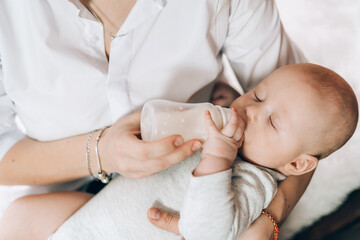 Young mother is holding her newborn baby in her arms and feeding from bottle. Love and care for children. Adoption of children. The child grows up without a father