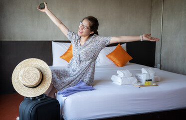 Happiness Asian tourist woman sitting on bed after check-in in hotel room. Conceptual of woman...