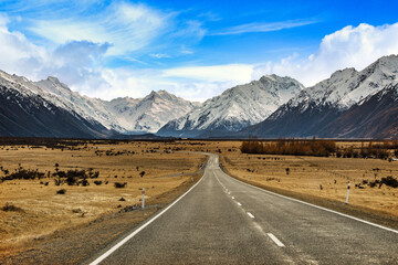 On the asphalt road to the big and tall Mountains  in winter, dry grass turns yellow in blue skies and beautiful clouds in the daytime in New Zealand National Parks.