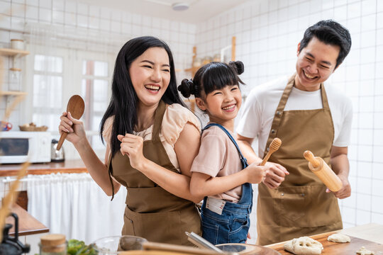 Asian family enjoy dancing and singing together while cooking at home.