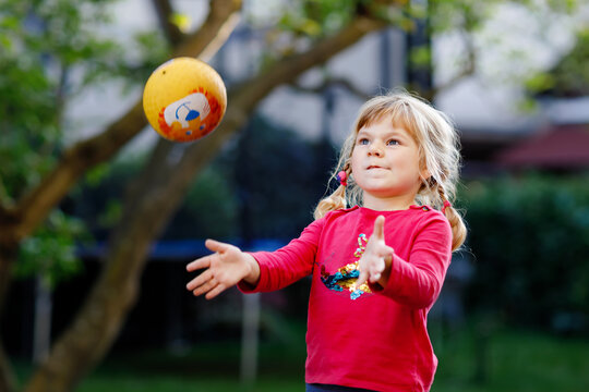 Little adorable toddler girl playing with ball outdoors. Happy smiling child catching and throwing, laughing and making sports. Active leisure with children and kids.