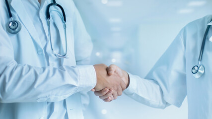 Medical Doctors senior shaking hands with young doctor on hospital background. Teamwork. Business and health care.