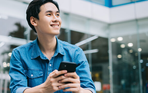 Image of young Asian man smiling and using smartphone