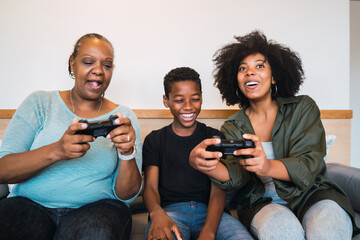 Grandmother, mother and son playing video games at home.