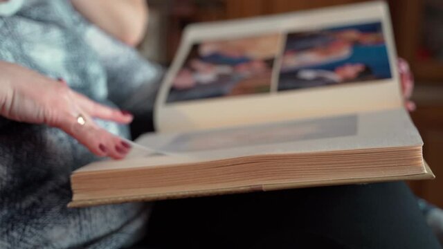 Elderly Woman Looking At Old Photo Album Close Up. Adult Female 60s Holding Nostalgic Memory In Photos In Cozy Modern Home. Casual Elderly Life And Wrinkled Skin Of Hands. Biography Or History Concept