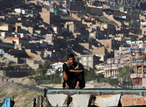 A truck driver sits on top of his car while waiting for customers to buy building materials in Kabul, Afghanistan