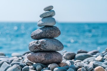 Pyramid stones on the seashore on a sunny day on the blue sea background. Happy holidays. Pebble beach, calm sea, travel destination. Concept of happy vacation on the sea, meditation, spa, calmness.