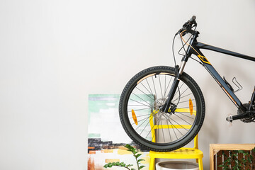 Modern bicycle on chair near white wall in room