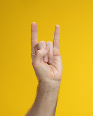 Folded fingers in shape of goat with two fingers raised up of man hand on yellow background