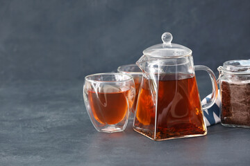 Teapot with hot tea and glasses on dark background