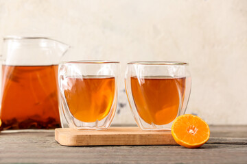 Teapot with hot tea, glasses and orange on wooden background