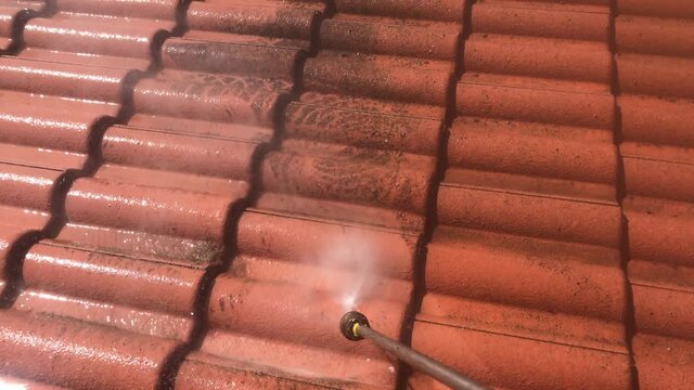 POV using a high pressure cleaning tool on a dirty roof tiling, removing moss and debris