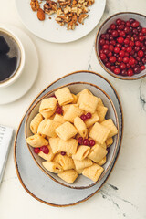 Bowl with tasty corn pillows, nuts and cranberries on light background