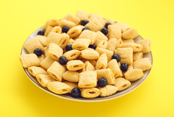 Plate with tasty corn pillows and blueberries on color background