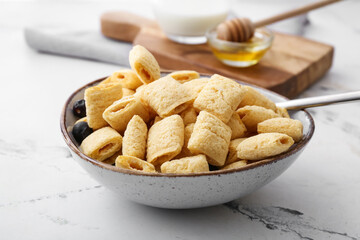 Bowl with tasty corn pillows and blueberries on light background
