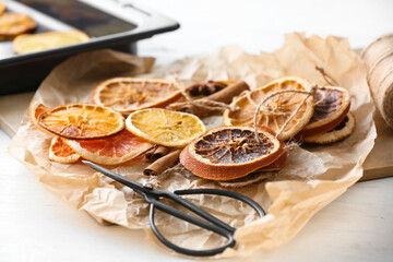 Scissors and dried orange slices on light background