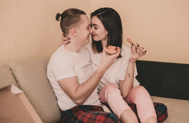 Couple in home clothes at home on bed eating pizza