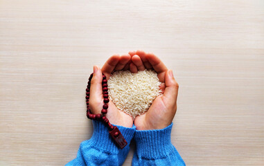 Women hands holding rice grain and prayer beads. Islamic zakat concept.
