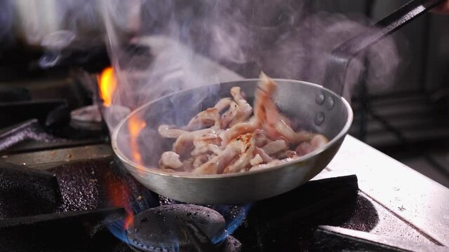 Making fried pork Brasso style - frying the pork meat strips in a pan, tossing and turning them, close up, camera slow orbit