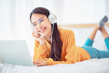 Happy woman relaxing while wearing headphones watching videos on laptop lying on a bed at home, Chill out and leisure concept