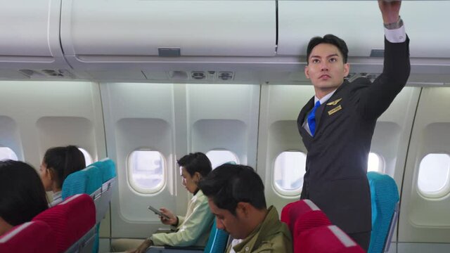 Asian flight attendant checking luggage compartment before departure.