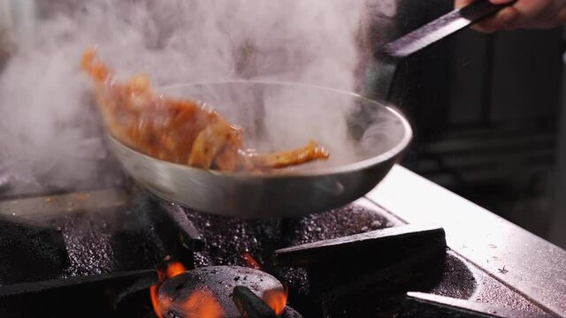 Making fried pork Brasso style - cooking the pork meat strips with the vegetable sauce, tossing the pan to mix the ingredients, close up, camera slow orbit