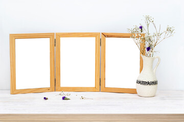 An empty mock-up of a wooden picture frame . A vase of dried white and purple flowers on a wooden table. Interior and home office design in the Scandinavian style.