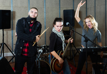 Fototapeta na wymiar Portrait of expressive active group of rock musicians posing with instruments in recording studio