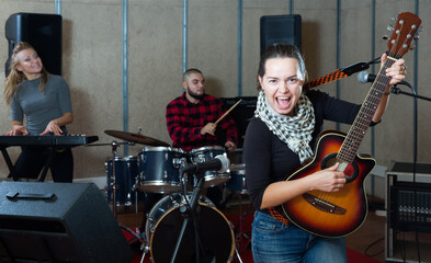 Rehearsal of music band. Young female guitar player and singer practicing with band members in recording studio