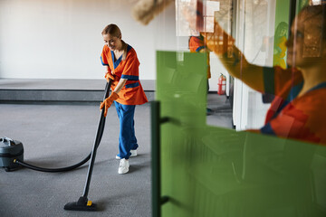 Janitor vacuuming the carpet in the presence of her colleagues