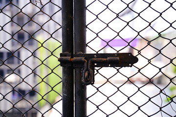 A grungy rusty old latch with A metal wire fence.