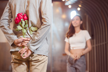 Obraz na płótnie Canvas Handsome young man standing with red roses behind the back on blurred happiness smiling girlfriend background..Man buys flowers for his dearest girlfriend on her success day