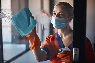 Woman in a mask and rubber gloves sanitizing office surfaces