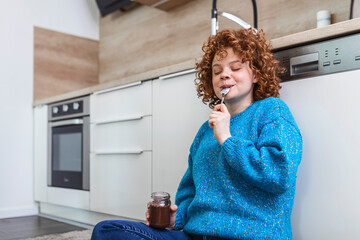 Cute ginger young woman in modern stylish clothes enjoying tasty chocolate spread with cute smile...